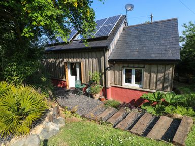 An exterior view of a wooden house with solar panels on the roof and a small outdoor seating area at The Studio at Dan y Garn in Newport Pembrokeshire
