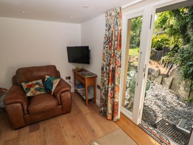A small seating area with a brown leather armchair, a wooden side table with board games and a wall-mounted TV next to glass doors opening to a garden at The Studio at Dan y Garn in Newport Pembrokeshire