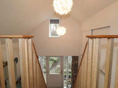 A stairway with wooden railings leading down to a door with glass panels and a pathway outside at The Studio at Dan y Garn in Newport Pembrokeshire