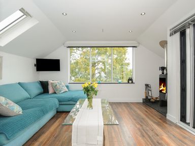 A living room with a blue sofa glass coffee table with flowers a fireplace and a large window at Moon's Cottage in Fowey