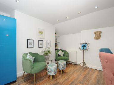 A seating area with green chairs and floral stools in a room with white walls and wooden floor at Moons Cottage in Fowey