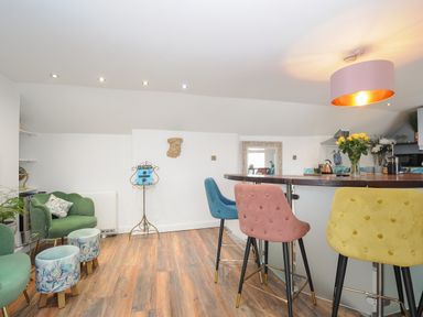 A dining area with colorful chairs and a bar counter with flowers at Moon's Cottage in Fowey