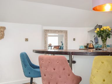 A kitchen area with colorful upholstered chairs around a wooden counter and a vase of yellow roses at Moons Cottage in Fowey