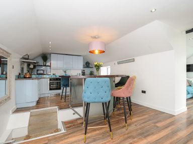 A kitchen with blue cabinets a wooden floor bar stools and stairs leading down at Moons Cottage in Fowey