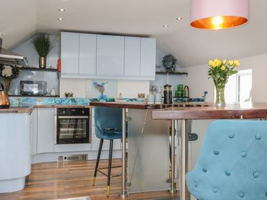 A kitchen with blue cabinets blue chairs wooden floor and yellow flowers in a vase at Moons Cottage in Fowey