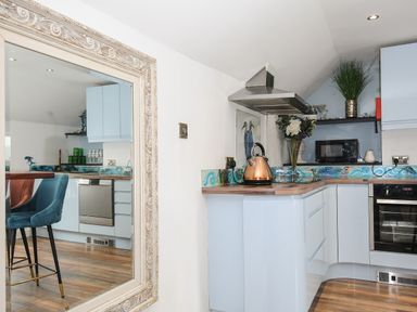 A kitchen with blue cabinets a copper kettle a microwave and a decorative mirror at Moon's Cottage in Fowey