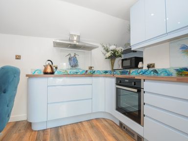 A kitchen with light blue cabinets wooden countertops a kettle oven microwave and a vase with flowers at Moon's Cottage in Fowey