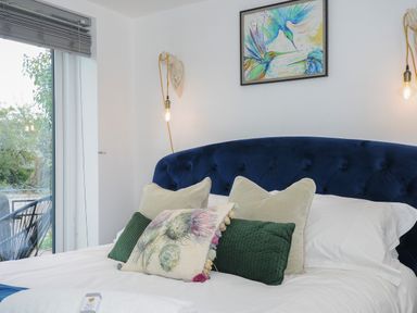 A bedroom with a bed with decorative pillows a framed bird painting on the wall and a window with blinds at Moons Cottage in Fowey