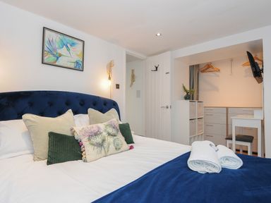 A bedroom with a blue upholstered bed and pillows a small desk wooden hangers and drawers at Moons Cottage in Fowey
