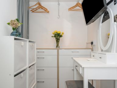 A dressing area with white drawers a vanity table with mirror wooden hangers and flowers in vases at Moons Cottage in Fowey