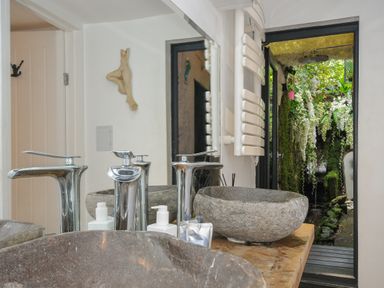 A bathroom with stone sinks and chrome faucets next to an open door showing an outdoor shower with flowers at Moons Cottage in Fowey