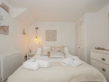 A bedroom with a bed with pillows and rolled towels and bedside table with a lamp at Moons Cottage in Fowey