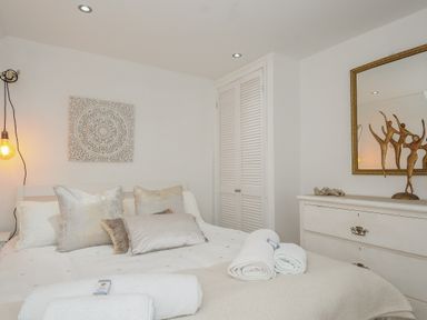 A bedroom with a bed, pillows, rolled towels, a dresser, a mirror, and wall decorations at Moons Cottage in Fowey