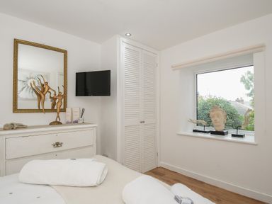 A bedroom with a white dresser with decorative sculptures a wall mounted tv a window with decorative items on the sill at Moons Cottage in Fowey