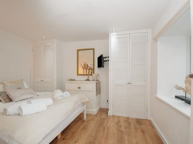 A bedroom with a bed with pillows and rolled towels a dresser with a mirror and sculptures and two closets at Moon's Cottage in Fowey