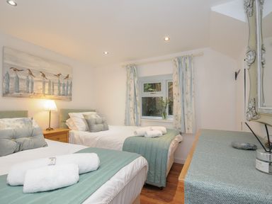 A bedroom with two single beds bedside table lamp window with curtains and a dresser at Moons Cottage in Fowey
