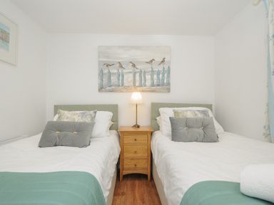 A bedroom with two single beds a wooden nightstand with a lamp between them and artwork of birds on a fence above the nightstand at Moons Cottage in Fowey