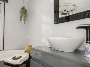 A bathroom with a white countertop basin a black faucet a mirror and a hanging plant at Moons Cottage in Fowey