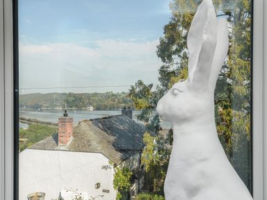 A large white rabbit sculpture by a window overlooking rooftops trees and a river at Moons Cottage in Fowey