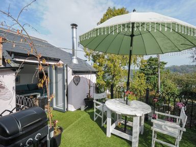 An outdoor patio area with a table chairs umbrella plants and a barbecue at Moons Cottage in Fowey