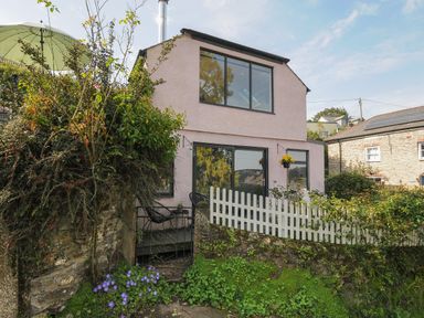 A two-story house with large windows and a white picket fence surrounded by plants and flowers at Moon's Cottage in Fowey