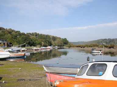 A river with several small boats moored along the shore and trees on the left side at Moons Cottage in Fowey