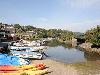 A river with kayaks and boats moored near houses and a bridge at Moons Cottage in Fowey