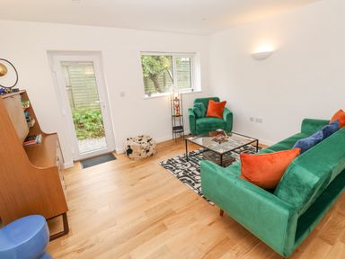 A sitting room with green sofa and armchair orange and blue cushions glass coffee table wooden floor and cabinet at James Place in Falmouth