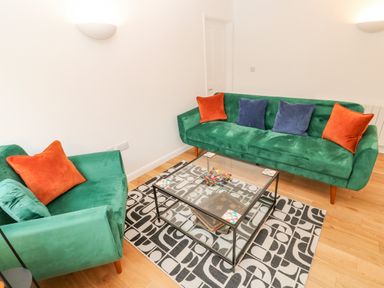 A sitting room with green sofas with orange and blue cushions a glass coffee table and a patterned rug at James Place in Falmouth