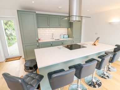A kitchen with green cabinets a white countertop island with black bar stools and a black cooktop at James Place in Falmouth