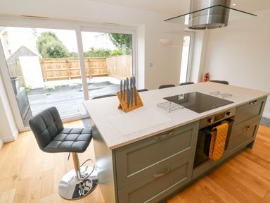A kitchen with an island featuring an electric cooktop an oven a knife block bar stools and sliding glass doors leading outside at James Place in Falmouth