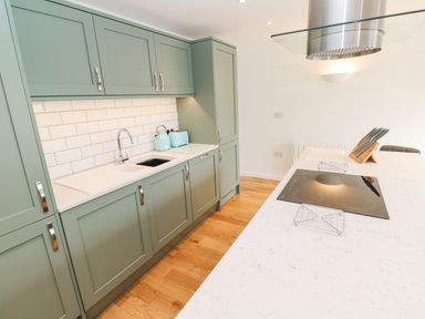 A kitchen with green cabinets a white countertop a sink stovetop and wooden floor at James Place in Falmouth
