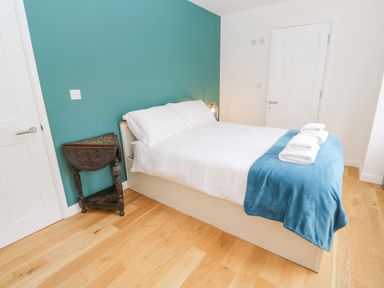 A bedroom with a double bed white bedding and blue blanket with towels on top a small wooden corner table and two white doors at James Place in Falmouth