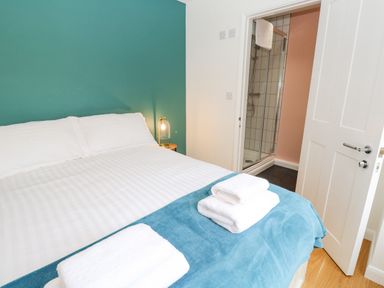 A bedroom with a bed with white and blue bedding and white towels on it and a door leading to a bathroom with a shower at James Place in Falmouth