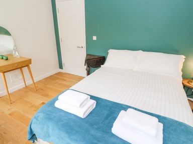 A bedroom with a double bed with white linens and folded towels on a blue blanket and a wooden table with a mirror at James Place in Falmouth