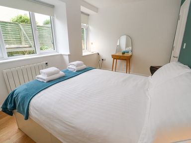 A bedroom with a bed covered in white linens and towels on a teal blanket a wooden dressing table with a mirror near the wall at James' Place in Falmouth