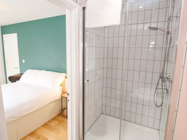 A bedroom with a bed and green wall next to a bathroom with a tiled shower at James Place in Falmouth