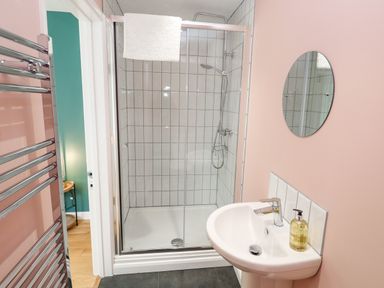 A bathroom with a glass enclosed shower a white sink with soap and an oval mirror at James Place in Falmouth