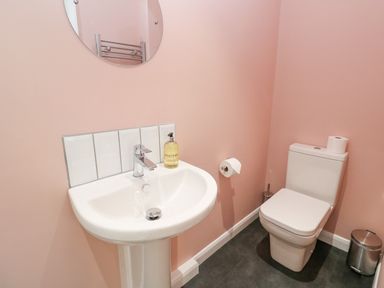 A small bathroom with a white sink and chrome faucet a round mirror and a white toilet with toilet paper at James Place in Falmouth