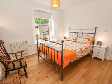 A bedroom with a metal frame bed with colorful bedding two bedside tables with lamps a wooden chair and a window with a mirror at James Place in Falmouth