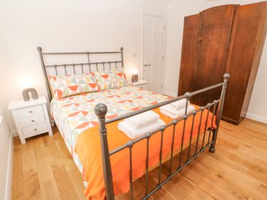 A bedroom with a metal bed frame patterned bed linen and orange blanket two white nightstands with lamps and a wooden wardrobe at James Place in Falmouth
