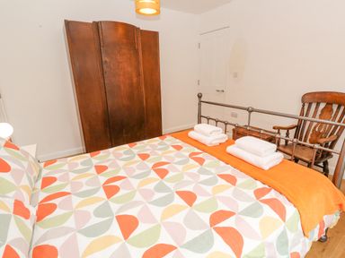 A bedroom with a patterned bedspread towels on a metal bed frame a wooden wardrobe and a wooden chair at James Place in Falmouth