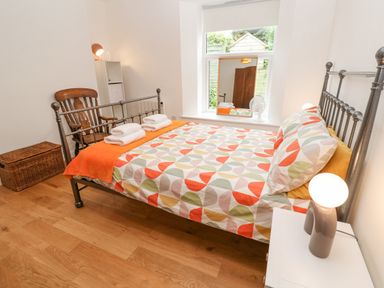 A bedroom with a metal bed frame, colorful bedspread, wooden chair, wicker basket, and window with a mirror at James Place in Falmouth