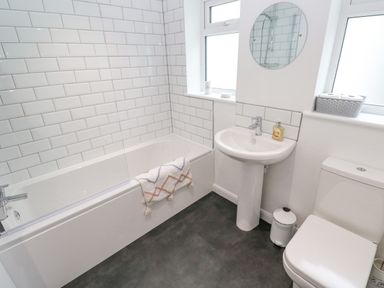 A bathroom with a bathtub a sink a toilet a round mirror and tiled walls at James Place in Falmouth