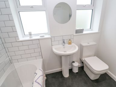 A bathroom with a bathtub, sink, toilet, round mirror, and two windows at James Place in Falmouth