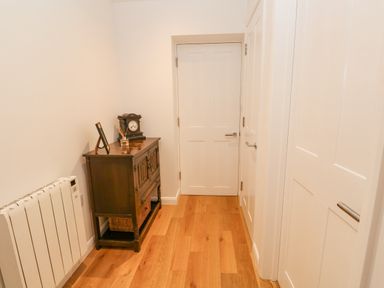 A hallway with wooden floor a dark wooden cabinet with clock and photo frame and white doors at James Place in Falmouth