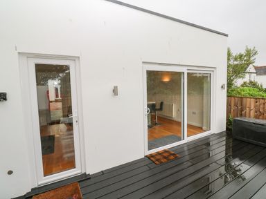 A patio area with two white framed glass doors and dark wooden decking at James Place in Falmouth
