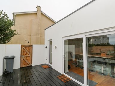 A small outdoor patio area with a wooden gate and black deck flooring at James Place in Falmouth