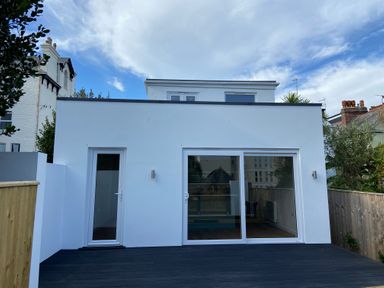 A white modern house exterior with a glass door and sliding patio doors leading to a dark deck at James Place in Falmouth