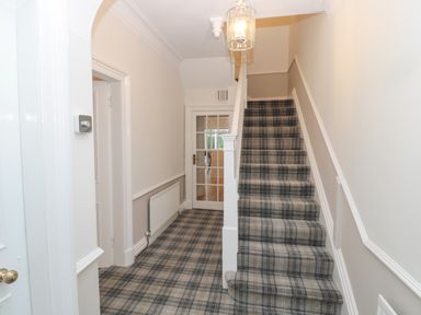 A hallway with a staircase covered in plaid carpet and a glass paneled door at St Aidans in Alnwick